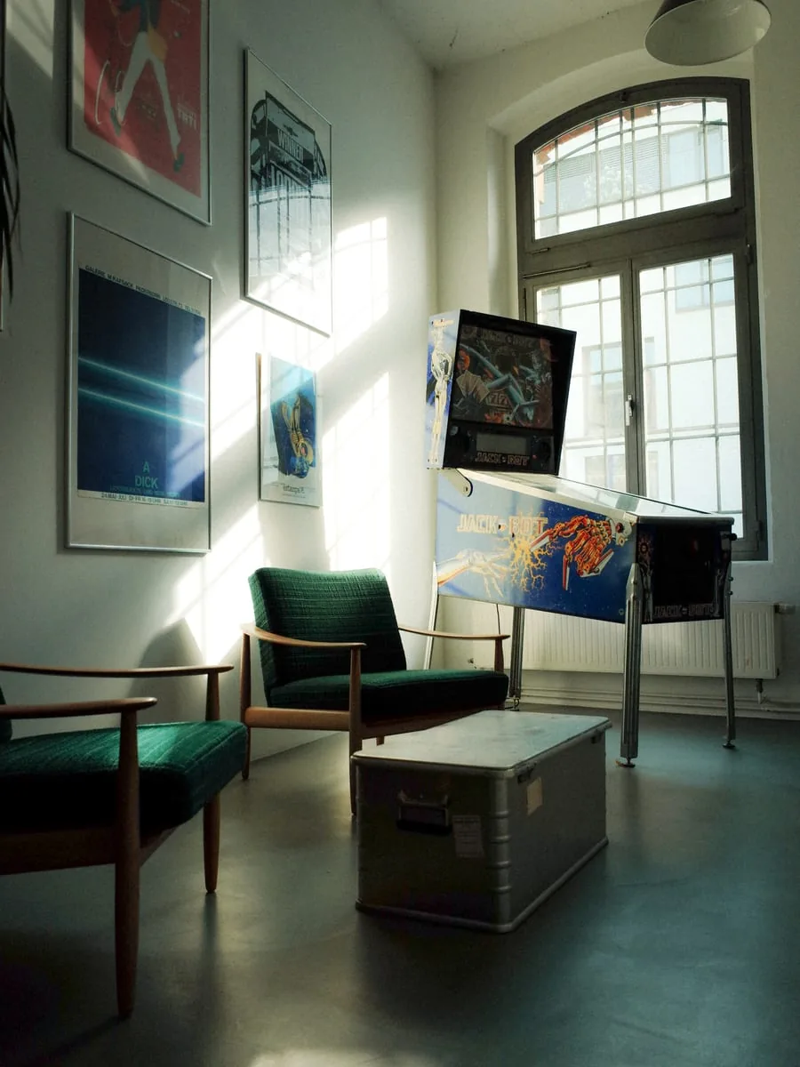 Das Studio im Krafthaus, Rheinauhafen Köln Büroecke im Krafthaus in Köln: zwei grüne Sessel und ein Flipperautomat vor einem hohen Rundbogenfenster, an der Wand Plakate