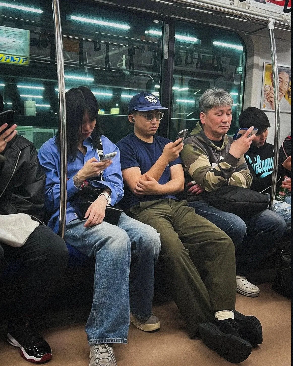 Das Publikum für laufenden Social-Media-Content: eine Sitzreihe in der U-Bahn, sechs Menschen dicht nebeneinander, fast jeder mit dem Smartphone in der Hand