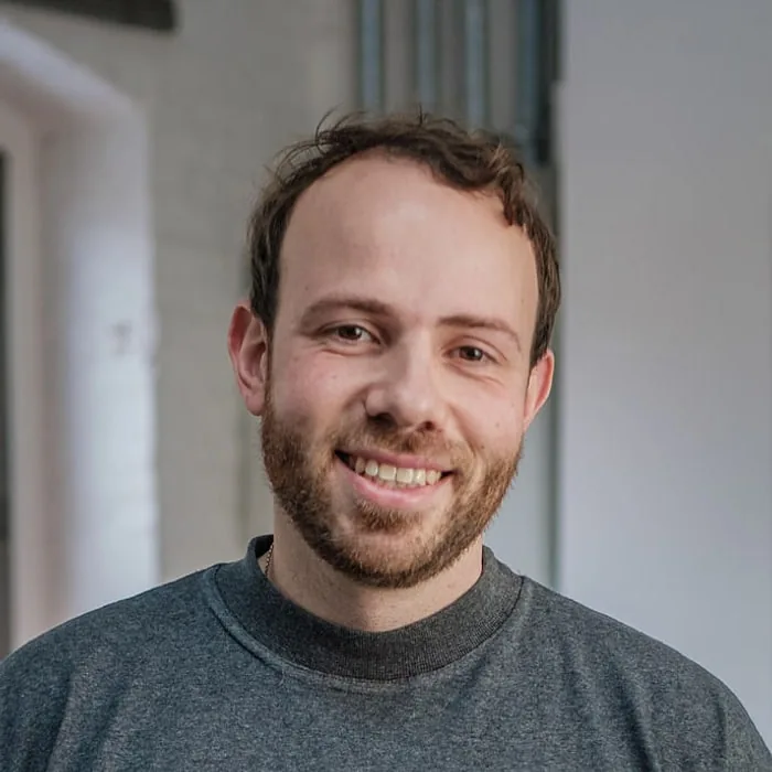 Cem-Pierre Schuch — Le Werk, Köln Cem-Pierre Schuch, Head of Production bei Le Werk in Köln, im grauen Shirt, lachend vor einer weißen Wand